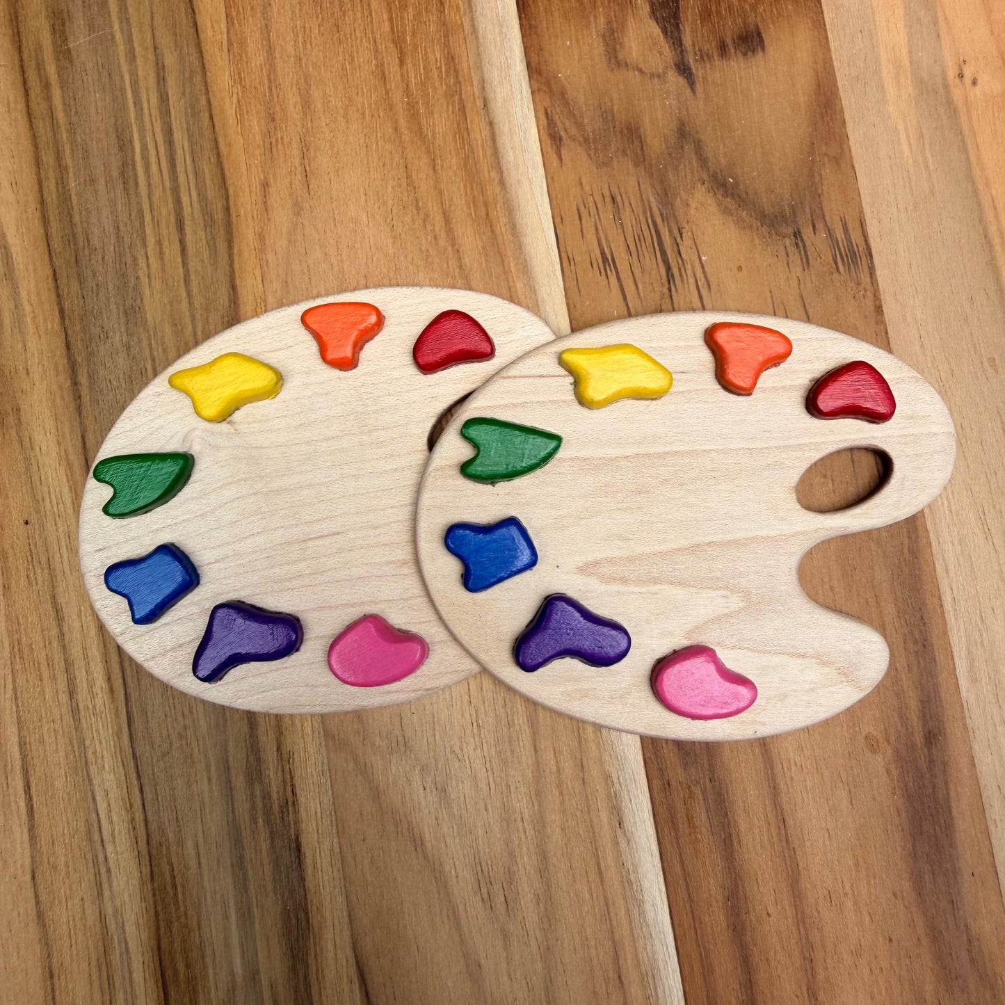 Two wooden paint palette magnets with colorful paint pieces embedded in them, arranged on a wooden surface. Shows how they look blank without engraving. 