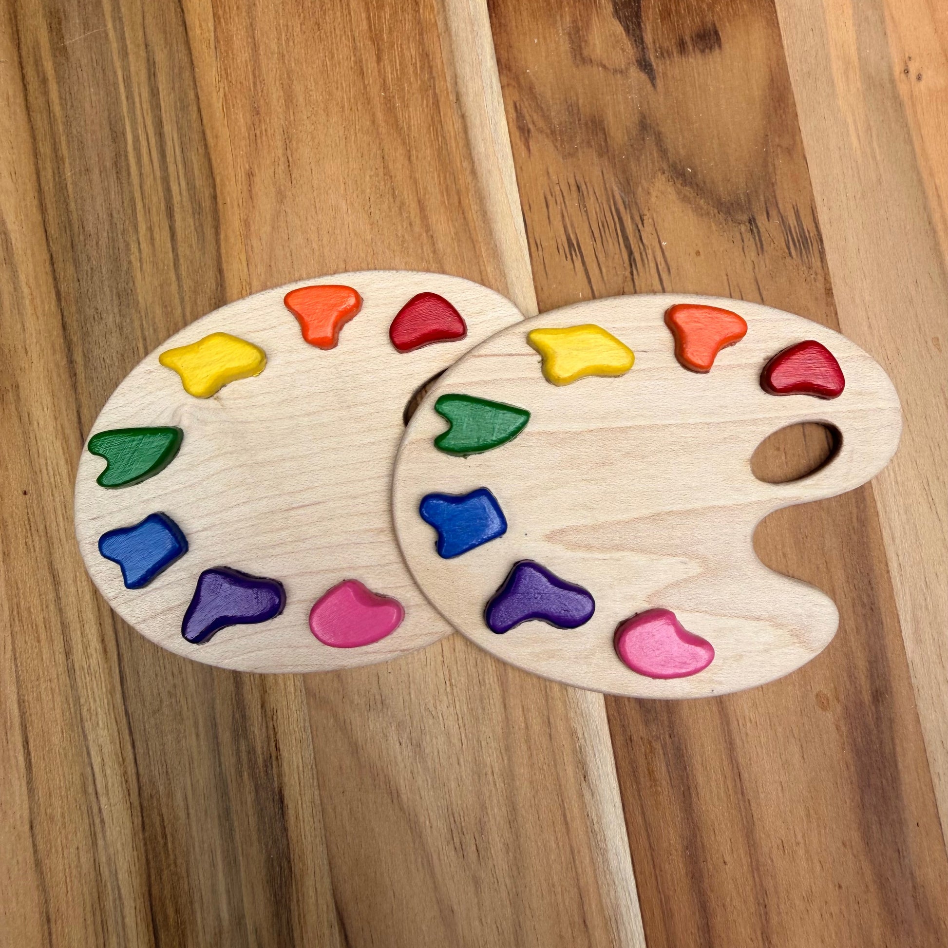 Two wooden paint palette magnets with colorful paint pieces embedded in them, arranged on a wooden surface. Shows how they look blank without engraving. 