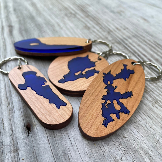 This image shows four different types of our popular lake keychains. All made from cherry plywood featuring a cobalt blue color wood for the lake inlay. Each keychain is adorned with a silver keyring.
